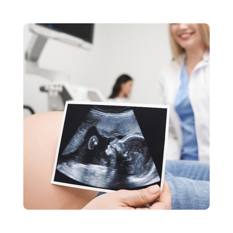 konsultacja z lekarzem w poradni ginekologicznej promed Ciężarna pacjentka trzymająca zdjęcie USG, w tle lekarka i sprzęt diagnostyczny