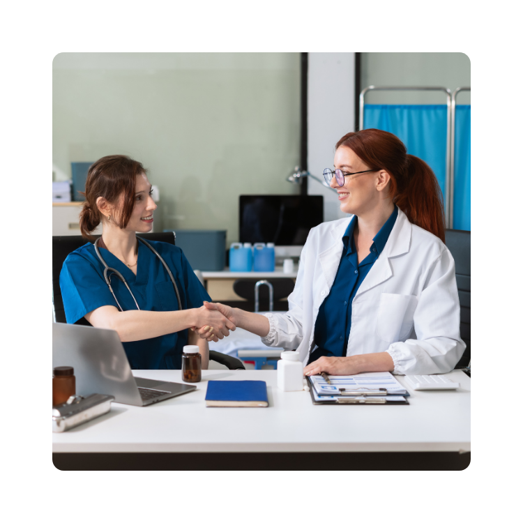 lekarki współpracujące podają sobie ręcę w gabinecie Dwie lekarki podające sobie ręce przy biurku – symbol współpracy i zaufania w placówkach PROMED