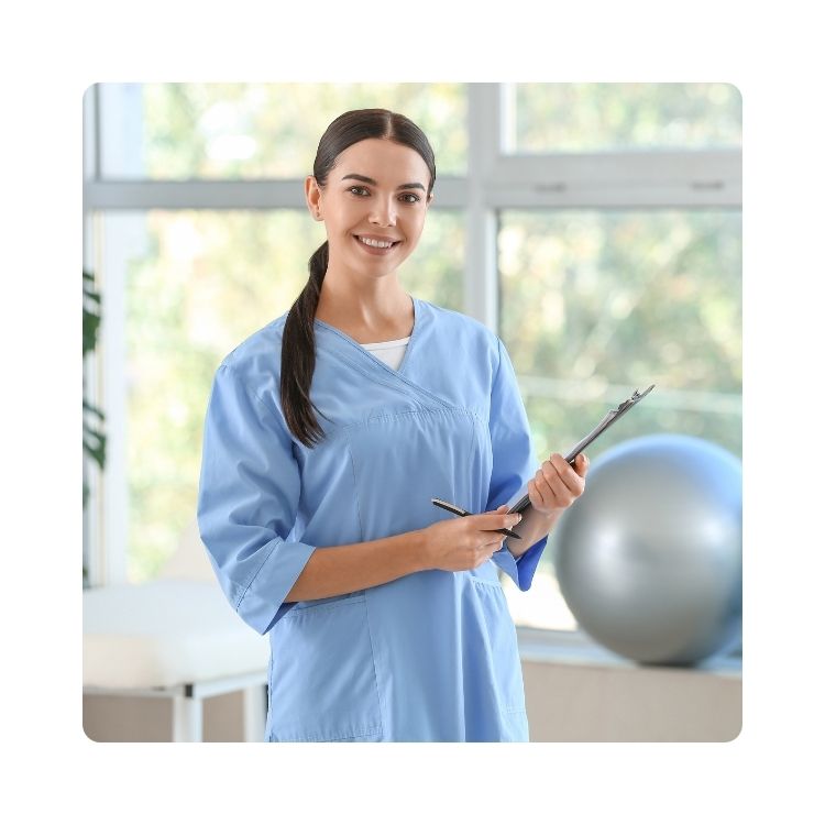 zdjęcie do poradni rehabilitacji (1) Fizjoterapeutka w niebieskim stroju medycznym trzyma dokumentację w gabinecie rehabilitacyjnym, w tle piłka do ćwiczeń